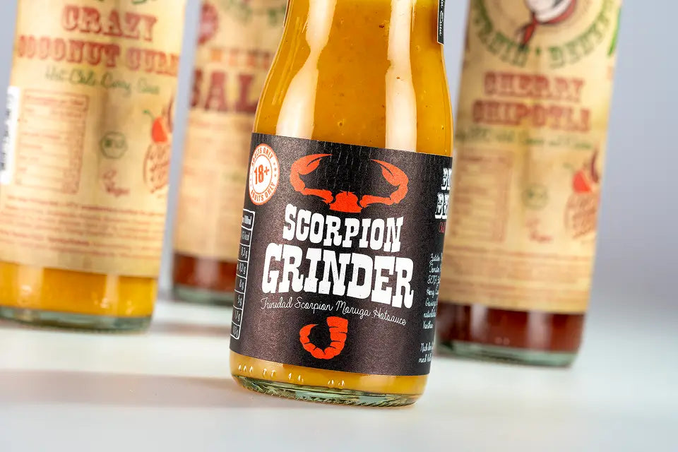 Dunkles Etikett auf einer Chilisaucen-Flasche, dahinter weitere Sorten